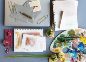 A birds eye view of cards, papers, and a painting palette. 